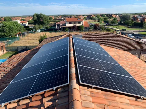 Amplia instalación de paneles solares en las dos vertientes de un tejado de teja, con jardín y piscina, en Aldeamayor de San Martín